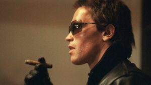 Arnold Schwarzenegger as the Terminator in the 1984 movie in sunglasses and holding a cigar halfway to his lips