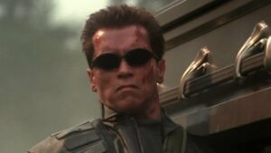 A screenshot of Arnold Schwarzenegger's Terminator from Terminator 3, wearing sunglasses and holding an ornate coffin on his shoulder