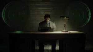 Alan Wake sits at a typewriter on a wooden desk with an older lamp and two round windows on the wooden-panelled wall behind him