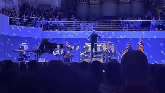 Foto tirada no show de Stardew Valley, Stardew Valley: Festival of Seasons, com projeção azul sobre a orquestra